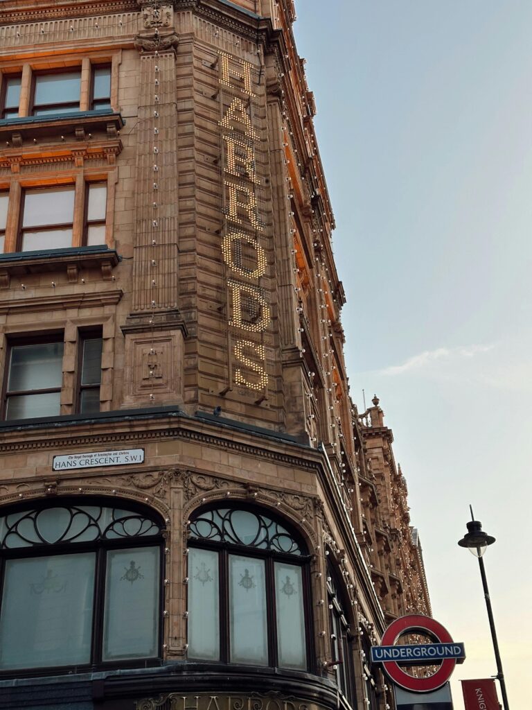 pexels-photo-28701067-28701067 View of Harrods in London with illuminated sign and Underground symbol against a clear sky.